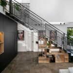 Čierne perforované kovové schodisko s drevenými policami pod ním, umiestnené pri vysokej čiernej skrini v modernom interiéri.