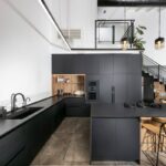 Moderná čierna kuchyňa s dlhým ostrovčekom, vstavanými spotrebičmi a bielou dlažbou na stene v otvorenom priestore.