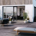 Biely rodinný dom s dreveným obkladom, terasou a posuvnými dverami v tmavom ráme.