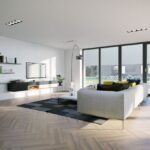 Moderná minimalistická obývačka s drevenou podlahou, sivou sedačkou a veľkými presklenými dverami.