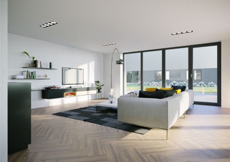 Moderná minimalistická obývačka s drevenou podlahou, sivou sedačkou a veľkými presklenými dverami.