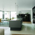 Priestranná moderná kuchyňa s tmavými skrinkami, ostrovčekom a veľkými presklenými posuvnými dverami.