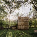 Sauna z upcyklovaných materiálov v prírodnom prostredí s kaďou na chladenie vedľa nej.