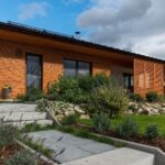 Montovaná drevostavba s chodníkom a upravenými záhonmi.