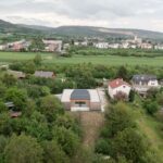 Moderný átriový dom s rovnou strechou a dreveným obkladom uprostred zelenej záhrady a okolitej zástavby.