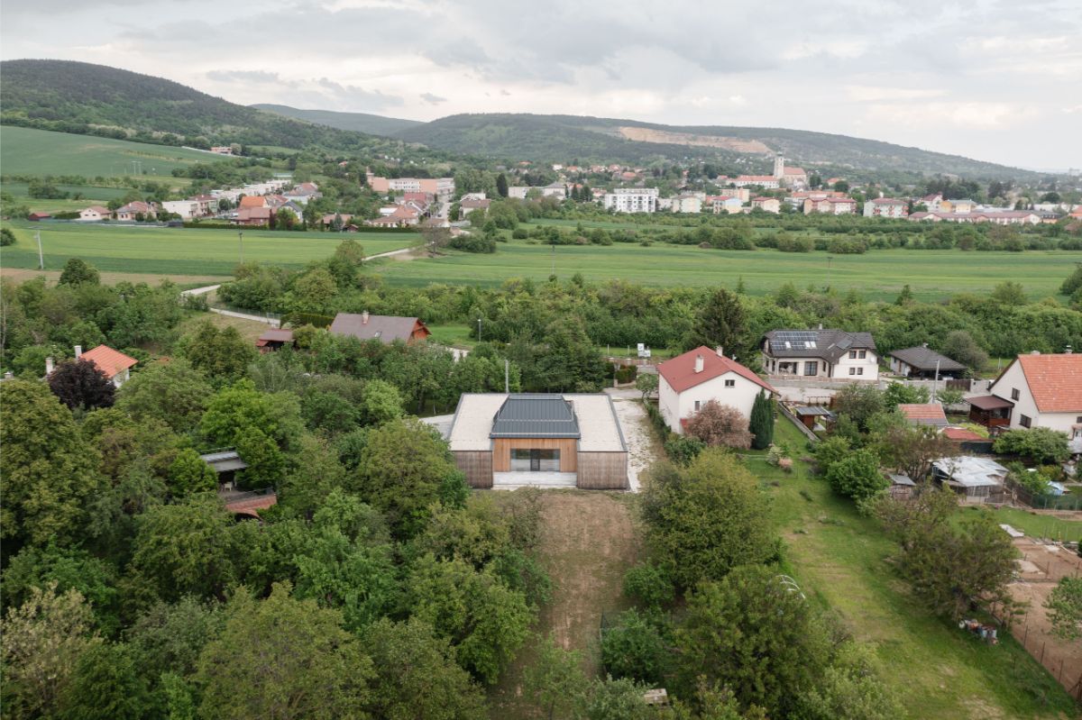 Moderný átriový dom s rovnou strechou a dreveným obkladom uprostred zelenej záhrady a okolitej zástavby.