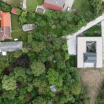 Pôdorysné usporiadanie átriového domu s centrálnym dvorom a svetlou plochou strechou v hustej záhrade.