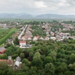 Panoráma Čachtíc s modernou drevostavbou, tradičnými domami a zelenými ovocnými sadmi.