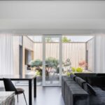 Pohľad z obývačky s minimalistickým moderným nábytkom do átria cez presklenú stenu.