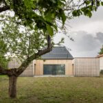 fasáda z prírodného dreva, tmavá sedlová strecha átriového domu a zatrávnená záhrada s ovocným stromom.