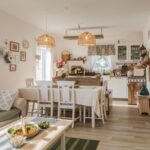 Otvorená bielo-drevená kuchyňa spojená s obývačkou v rustikálnom štýle, s bielym jedálenským stolom a zelenou kachľovou pecou.