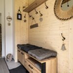 Vstupná chodba s dreveným obkladom, skrinkou na topánky a čiernymi mäkkými sedákmi, s jutovým zrkadlom a vešiakmi.