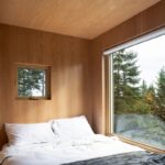 Svetlá spálňa s obkladom zo svetlého dreva, s veľkým aj menším oknom, biela posteľná bielizeň.