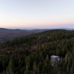 Interiér z podkrovia s bieleným dreveným obkladom, galériou, bielou záclonou a rebríkom na galériu.