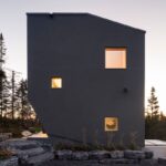 Bočná fasáda tmavej chaty v prírode s nepravidelnými oknami.