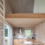 Minimalistický priestor kuchyne a jedálne so svetlým dreveným obložením a schodmi na medziposchodie.