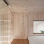 Svetlé podkrovie s bieleným dreveným obkladom, manželskou posteľou na drevenom pódiu a bielym rebríkom.