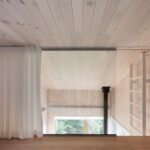 Interiér z podkrovia s bieleným dreveným obkladom, galériou, bielou záclonou a rebríkom na galériu.