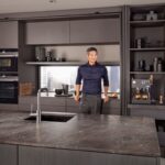 Muž opierajúci sa o modernú kuchynskú linku v tmavohnedej farbe.