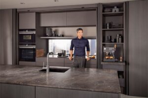 Muž opierajúci sa o modernú kuchynskú linku v tmavohnedej farbe.