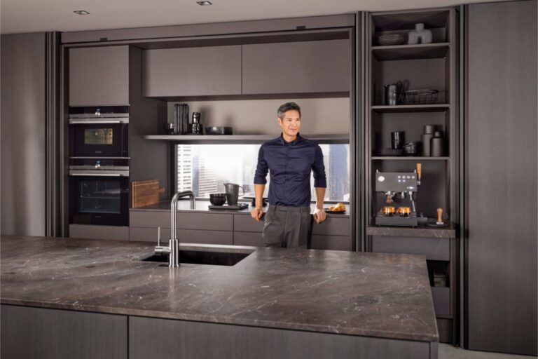 Muž opierajúci sa o modernú kuchynskú linku v tmavohnedej farbe.