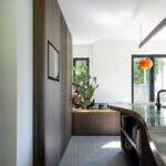 Chodba s vysokou dyhovanou drevenou skriňou s TV a tmavou pracovnou doskou v kuchyni.