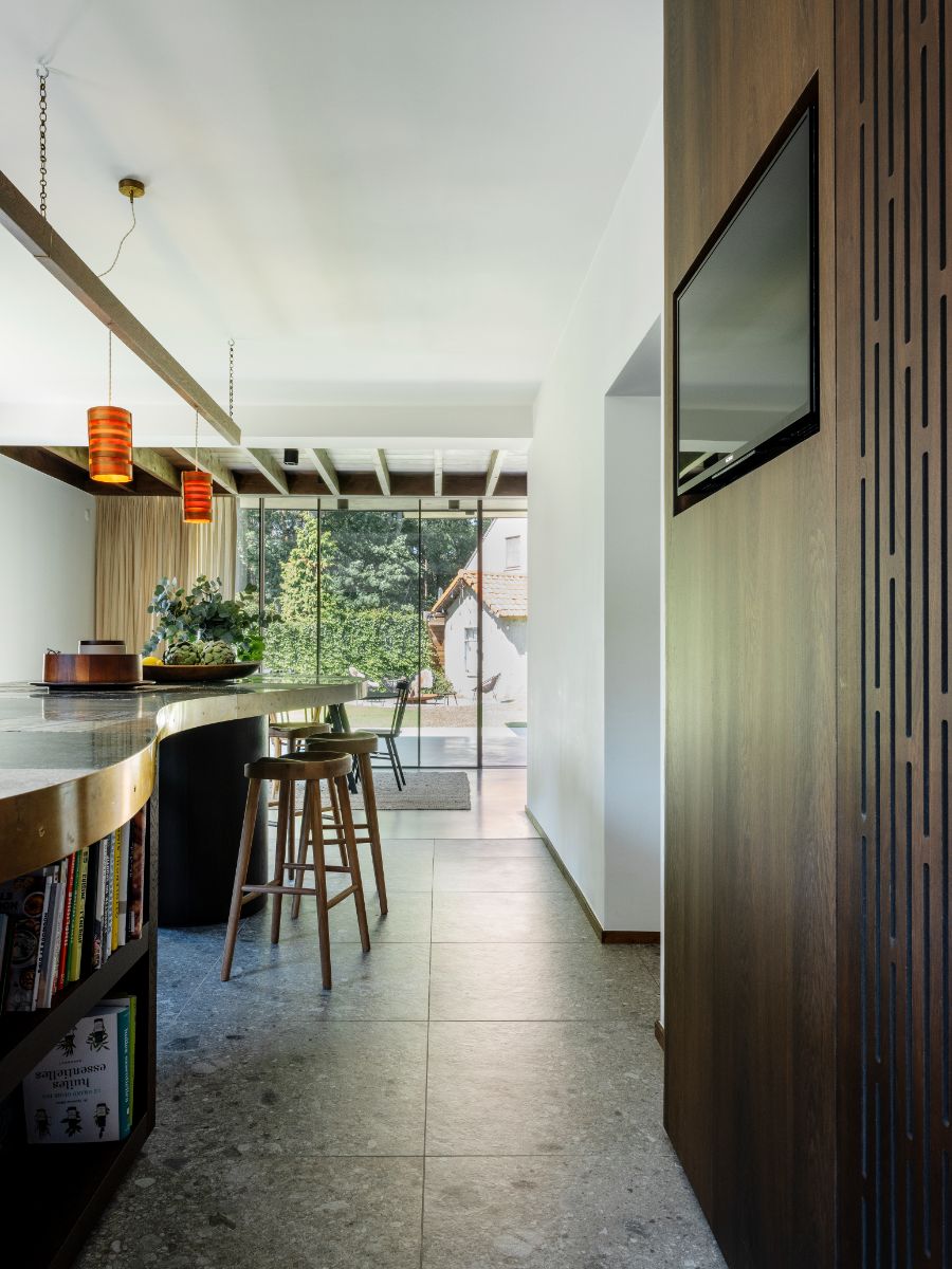 Kuchynský ostrovček s tmavou mramorovou doskou, drevenými barovými stoličkami a oranžovými lampami.