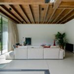 Obývačka s veľkým bielym gaučom pod tmavým dreveným trámovým stropom a širokými sklenými dverami.