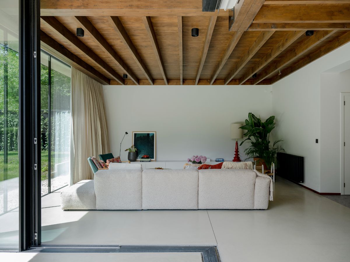 Obývačka s veľkým bielym gaučom pod tmavým dreveným trámovým stropom a širokými sklenými dverami.