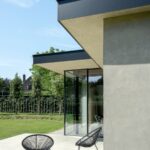 Moderná fasáda domu s plochou tmavou strechou a terasou s exteriérovými kreslami.