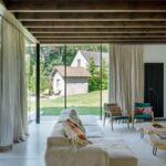 Moderná obývačka s béžovou sedačkou, zelenými kreslami a drevenými stolíkmi pod trámovým stropom.