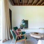 Obývačka so zelenými kreslami, prírodnými stolíkmi a bielou stenou pod tmavým trámovým stropom.