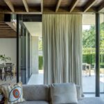 ohová béžová sedačka s vankúšmi a výhľadom na jedáleň s čiernym stolom cez svetlé závesy.