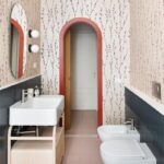 Kúpeľňa s ružovou dlažbou a tapetou so vzorom konárikov a tmavomodrými obkladmi. a oblúkový priechod s červeným lemom.