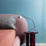 Detail časti postele s bouclé čalúnením, nočným stolíkom a stolnou lampou.