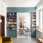 Svetlá obývacia izba s zamatovou sedačkou a tyrkysovou knižnicou a terrazzo podlahou.