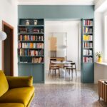 Svetlá obývacia izba s zamatovou sedačkou a tyrkysovou knižnicou a terrazzo podlahou.