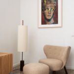 Béžové kreslo a taburet s tmavými nohami na terrazzo podlahe.