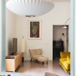 Obývacia izba s béžovým kreslom, drevenou skrinkou a žltou sedačkou.