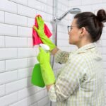 Žena pri umývaní obkladačiek sprchového kúta.