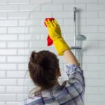 Žena pri čistení skla sprchového kúta.