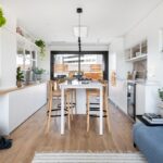 Otvorený priestor s kuchyňou a jedálňou, bielymi skrinkami a drevenou podlahou, s prechodom na terasu.