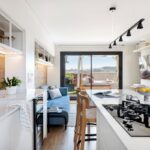 Otvorená moderná kuchyňa s bielymi skrinkami, ostrovčekom s varnou doskou a výhľadom cez sklenené dvere na terasu.