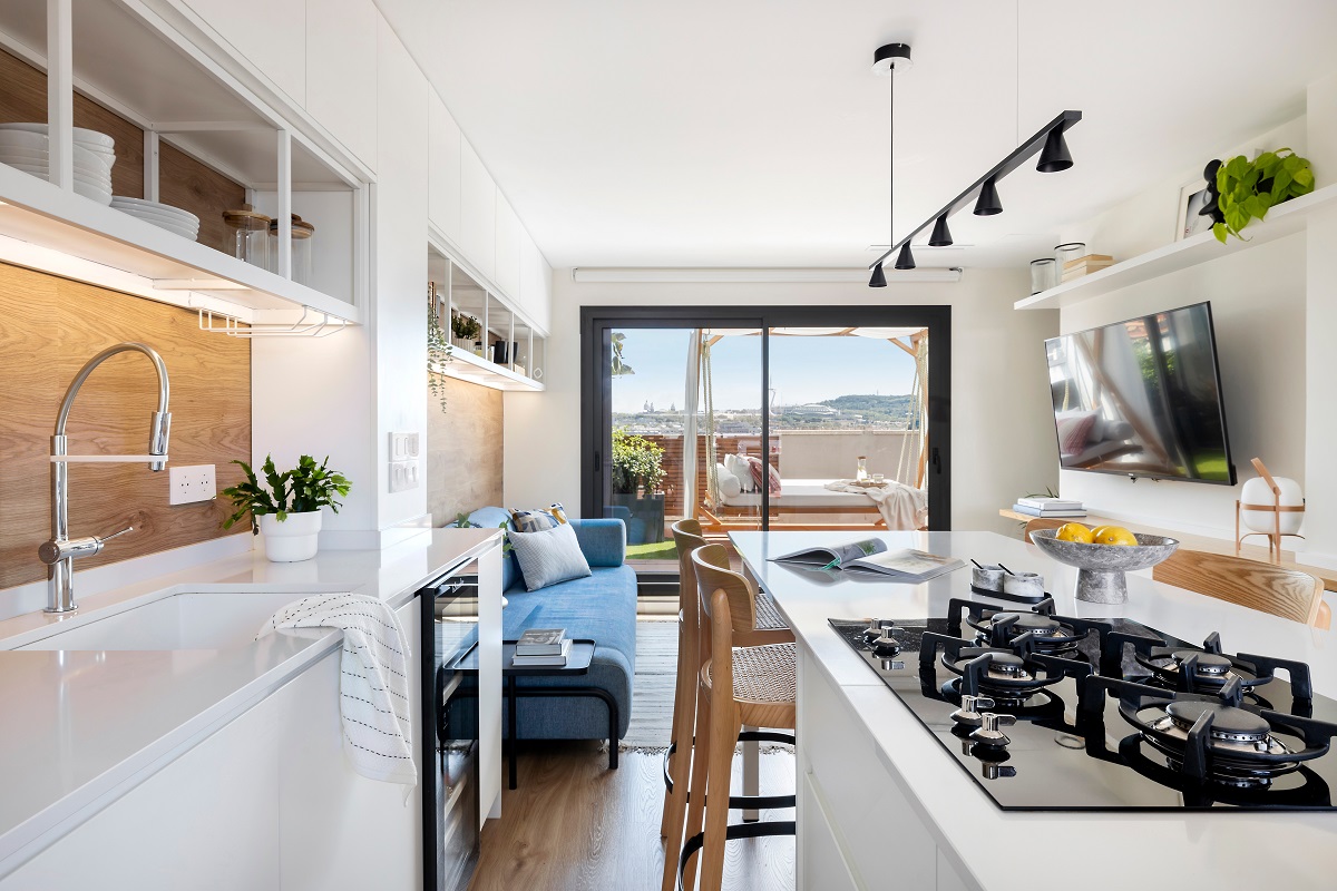 Otvorená moderná kuchyňa s bielymi skrinkami, ostrovčekom s varnou doskou a výhľadom cez sklenené dvere na terasu.
