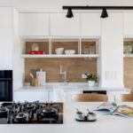 Moderná kuchyňa s bielymi skrinkami, dreveným obkladom a čiernou plynovou varnou doskou na ostrovčeku.