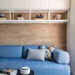 Obývačka so stenou so svetlým dreveným obkladom, modrou sedačkou a bielou policovou zostavou s dekoráciami.