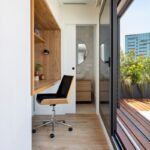 Svetlý minimalistický pracovný kútik s dreveným vstavaným stolom a čiernou stoličkou, s východom na terasu.