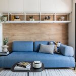 Obývačka so stenou so svetlým dreveným obkladom, modrou sedačkou a bielou policovou zostavou s dekoráciami.