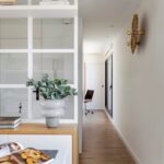 Svetlá dlhá chodba s drevenou podlahou, bielou stenou a vysokým prechodom do vedľajšej miestnosti.