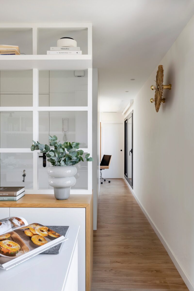 Svetlá dlhá chodba s drevenou podlahou, bielou stenou a vysokým prechodom do vedľajšej miestnosti.